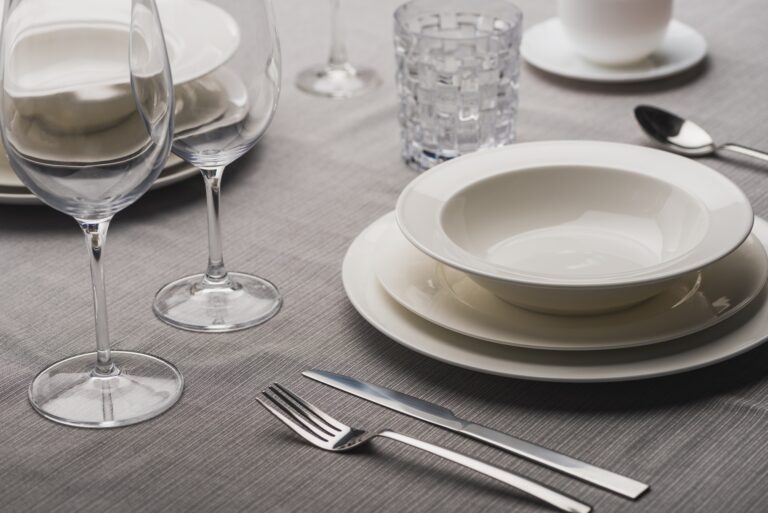 Serving dinnerware with cutlery and glasses on grey linen tablecloth